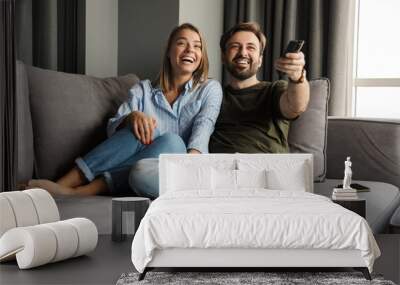 Photo of joyful couple watching TV and using remote control Wall mural