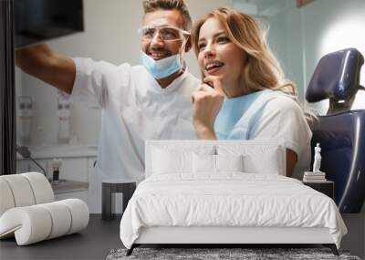 Photo of joyful woman sitting in medical chair at dental clinic while doctor fixing her teeth Wall mural