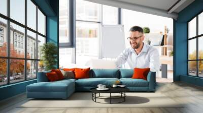 Photo of joyous office man 30s in white shirt sitting at desk and working on laptop in business centre Wall mural