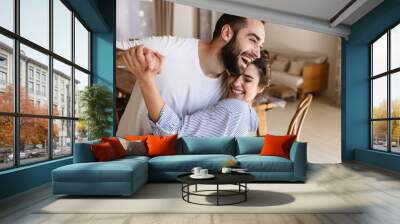 Photo of laughing brunette couple in love smiling while hugging together in apartment Wall mural