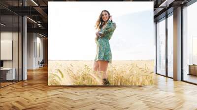 Photo of pleased cute woman smiling while walking on wheat field Wall mural