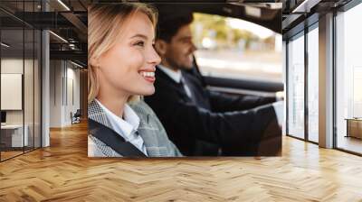 Photo of pleased man and woman talking and smiling while driving in car Wall mural