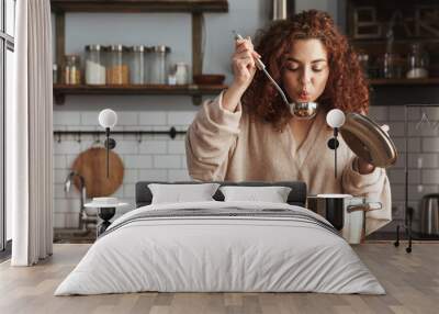 Photo of pretty caucasian woman holding cooking ladle spoon while eating soup at home Wall mural