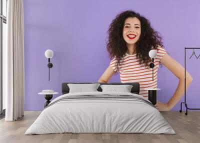 Photo of pretty hipster woman with curly hair in summer wear smiling and looking at you, isolated over violet background in studio Wall mural