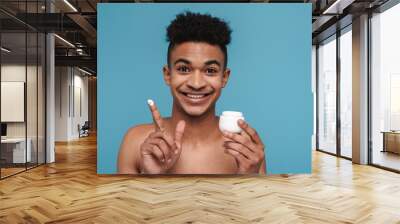 Photo of shirtless african american man smiling and applying face cream Wall mural