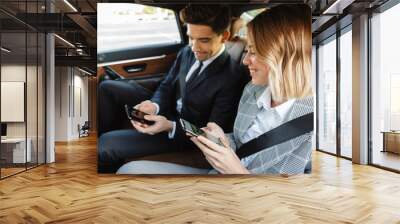 Photo of smiling man and woman using cellphones while going in car Wall mural