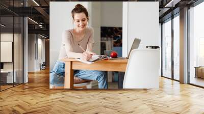 Photo of smiling student girl in earphones doing homework with laptop Wall mural