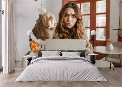 Photo of strict woman in sweater looking on camera and gesturing finger on you with persistent gaze, while using laptop in cafe Wall mural