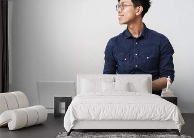 Photo of successful asian businessman sitting at table and holding smartphone while working with laptop in office Wall mural