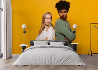 Photo of unhappy students man and woman 16-18 standing back to back with arms folded in quarrel, isolated over yellow background Wall mural