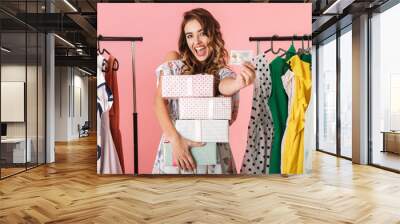 Photo of young lady with purchase standing in store near clothes rack and holding credit card Wall mural