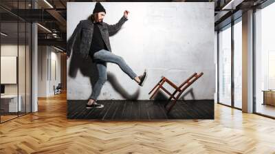 Portrait of a bearded hipster man kicking chair with foot Wall mural