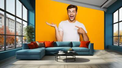 Portrait of a cheerful young man pointing fingers away Wall mural