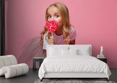 Portrait of a pretty little girl holding heart shaped lollipop Wall mural