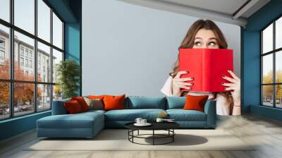 Portrait of a pretty young girl hiding behind an open book Wall mural