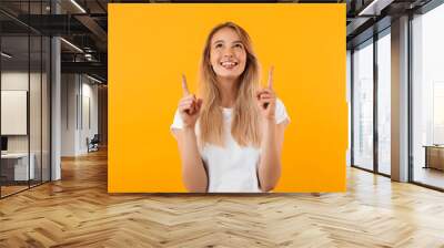 Portrait of a smiling young blonde girl pointing up Wall mural