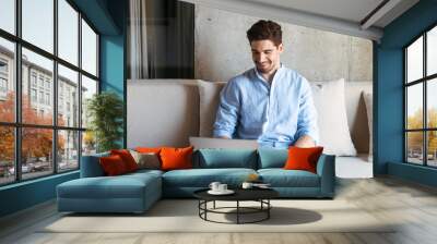 Portrait of a smiling young man using laptop computer Wall mural