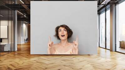 Portrait of a surprised young woman pointing fingers up Wall mural