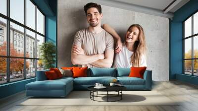 Portrait of adorable caucasian couple man and woman in basic clothing posing together at camera with happy smile, isolated over concrete gray wall indoor Wall mural