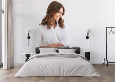 Portrait of adorable smiling woman with long brown hair holding and looking at silver laptop, isolated over white background in studio Wall mural