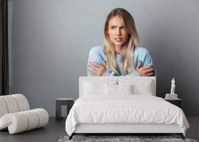 Portrait of an annoyed young blonde girl shaking from cold Wall mural