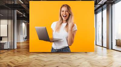 Portrait of an excited young blonde girl holding laptop Wall mural