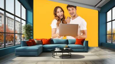 Portrait of beautiful couple man and woman in basic t-shirts smiling while standing together with silver laptop Wall mural