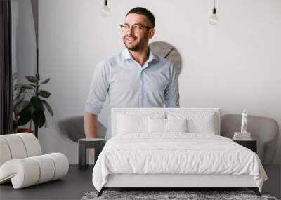 Portrait of businesslike man wearing white shirt standing in office interior, and looking aside with happy smile Wall mural