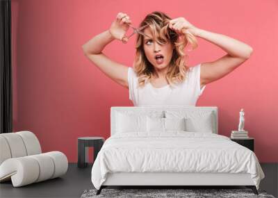 Portrait of caucasian blond woman 20s wearing casual t-shirt cutting her hair with scissors Wall mural