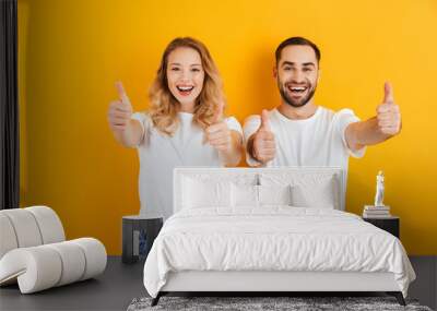 Portrait of cheerful young couple man and woman in basic t-shirts smiling and showing thumbs up at camera Wall mural