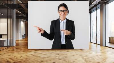 Portrait of european businesswoman 30s in formal wear and eyeglasses pointing fingers aside, isolated over white background Wall mural