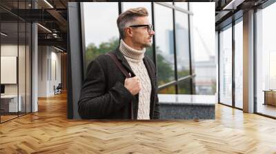 Portrait of european man 30s wearing eyeglasses, walking through city street near the building Wall mural