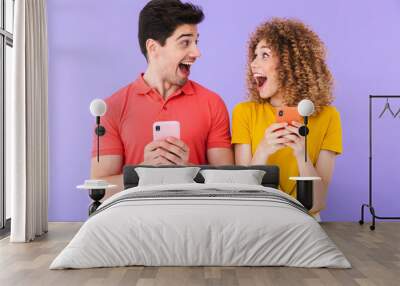 Portrait of excited caucasian people man and woman in basic clothing rejoicing while using cellphones together Wall mural