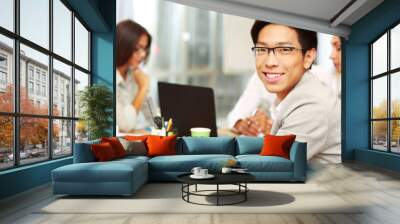 Portrait of happy businessman sitting in front of colleagues Wall mural