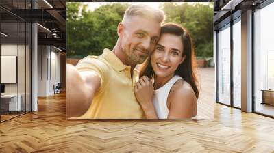 Portrait of happy middle-aged couple taking selfie photo and hugging while walking in summer park Wall mural