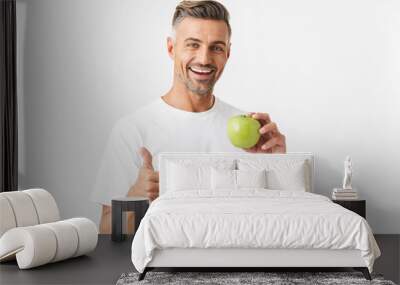 Portrait of healthy man 30s having bristle in casual t-shirt posing on camera and holding green apple in hand Wall mural