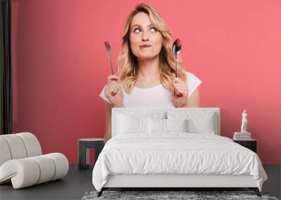 Portrait of thoughtful blond woman 20s wearing body measuring tape around waist holding spoon and fork Wall mural