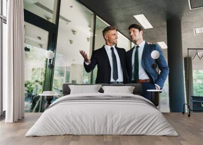 Portrait of two happy businessmen partners talking together while walking outside job center during working meeting Wall mural