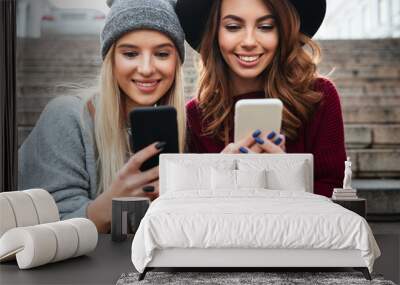 Portrait of two smiling pretty girls using mobile phones Wall mural