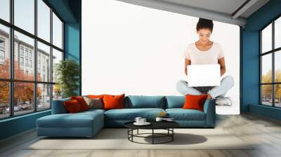 Portrait of woman in casual sitting on floor in lotus pose and holding laptop, isolated over white background Wall mural