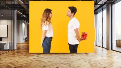 Portrait of young couple in basic t-shirts standing face to face while man holding and giving present box to woman Wall mural