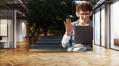 Portrait of young curly boy in glasses holding video conference Wall mural