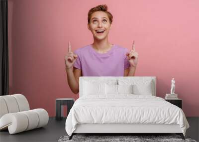 Portrait of young short-haired beautiful smiling woman pointing upwards Wall mural