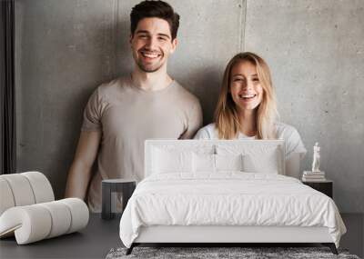 Portrait of young smiling people guy and girl 20s in basic clothing posing together at camera with happy look, isolated over concrete gray wall indoor Wall mural