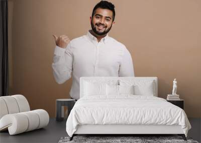 Positive indian man pointing finger at copy space isolated over beige background Wall mural