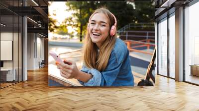 Positive young teenage girl outside in park holding mobile phone. Wall mural