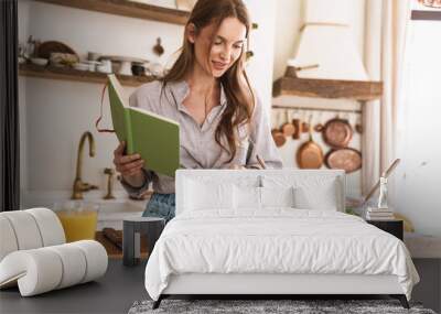 Pretty lady indoors at the kitchen cooking holding notebook. Wall mural