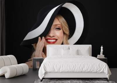 Pretty young happy cheerful blonde woman with bright makeup red lips posing isolated over black wall background wearing hat. Wall mural