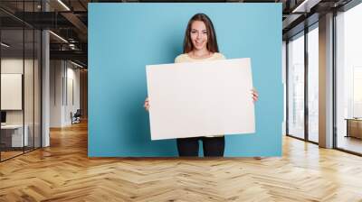 Pretty young woman holding empty blank board over blue background Wall mural