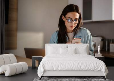 Serious charming woman using smartphone while working with laptop Wall mural